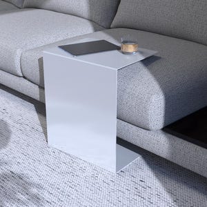May include: A white side table with a curved edge sits next to a gray couch. The table has a laptop and a glass on top.