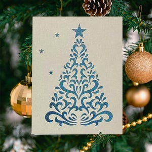 Peut inclure: Carte de Noël avec un motif d'arbre décoratif bleu et une étoile. La carte est placée devant un sapin de Noël décoré avec des boules et des pommes de pin.