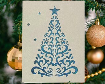 May include: A Christmas card featuring a blue decorative tree design with a star on top. The card is set against a backdrop of a decorated Christmas tree with ornaments and pine cones.