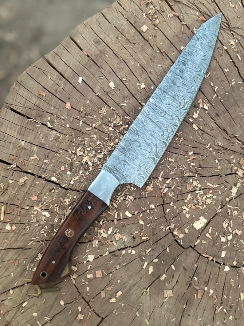 May include: A Damascus steel chef's knife with a dark wood handle. The blade has a unique swirling pattern. The knife is resting on a weathered wooden surface, showcasing the craftsmanship and design of the kitchen tool.