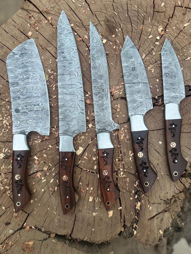 May include: A set of six Damascus steel knives with wooden handles. The blades have a unique patterned design. The handles are dark brown with decorative metal accents. The knives are arranged on a rough-hewn wooden surface.