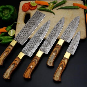 May include: A set of six kitchen knives with patterned steel blades and wooden handles. The knives have brass bolsters and are arranged on a wooden cutting board with vegetables.