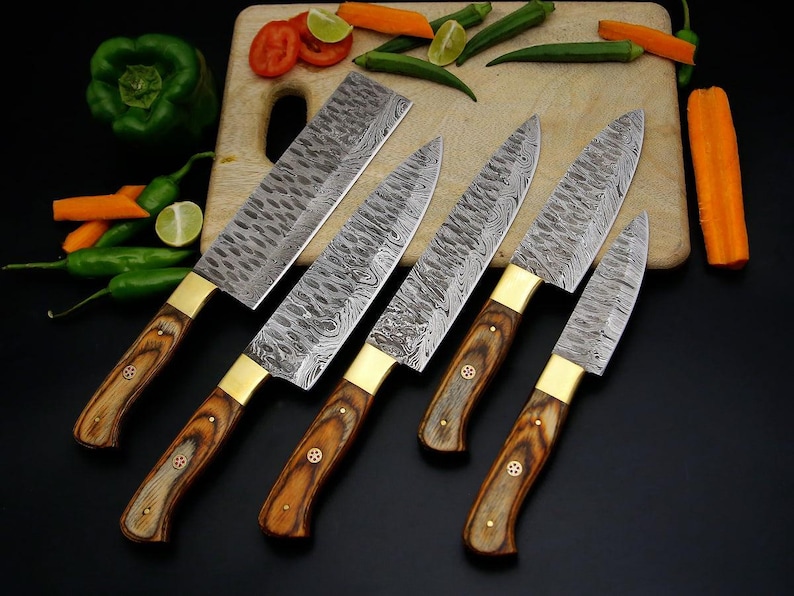 May include: A set of six kitchen knives with patterned steel blades and wooden handles. The knives have brass bolsters and are arranged on a wooden cutting board with vegetables.