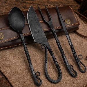 Puede incluir: Un juego de cuatro utensilios de metal forjado negro que incluye una cuchara, un cuchillo, un tenedor de dos puntas y un pincho, cada uno con un mango trenzado y un extremo rizado. El texto Chilgoza está grabado en los mangos de los utensilios.