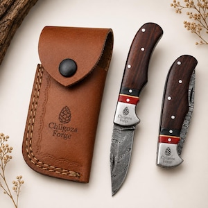 May include: A brown leather sheath with a snap closure and a Chilgoza Forge logo, alongside two folding knives with dark wood handles, red and black accents, and Damascus steel blades featuring the Chilgoza Forge logo on the metal bolsters.