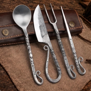 May include: A set of four metal utensils including a spoon, a knife, a two-pronged fork, and a skewer, each featuring a twisted handle and a curled end. The items are engraved with the text Chilgoza and are displayed with a brown leather case.