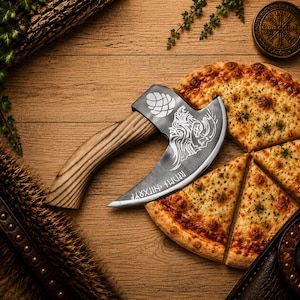 K&ouml;nnte beinhalten: Ein Pizzaschneider in Form einer kleinen Axt mit geschwungenem Holzgriff und Metallklinge. Die Klinge ist mit einem Totenkopf, einem Tannenzapfen und Runenschrift graviert. Der Schneider liegt neben mehreren St&uuml;cken K&auml;sepizza auf dem Tisch.