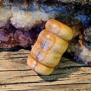 Puede incluir: Un rodillo de madera, de forma cilíndrica, tallado a mano, de color marrón y beige, con un acabado liso y pulido.