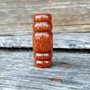 May include: A close-up of a wooden knob with a reddish-brown color and a textured surface. The knob has a cylindrical shape with three raised rings.