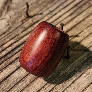 May include: A handcrafted, reddish-brown wooden pipe with a smooth, polished finish. The pipe has a rounded, barrel-like shape with a wide opening at the top. The wood grain is visible, adding to the natural aesthetic. The pipe is designed for smoking.