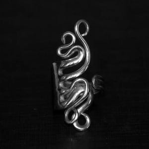 May include: A silver ring featuring a distinctive, abstract design that resembles a swirling, organic shape.