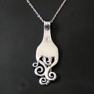 May include: A silver necklace with a pendant made from a repurposed fork. The fork tines have been twisted into a decorative swirl design.