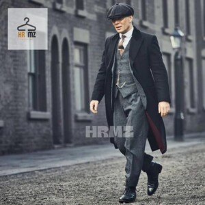 May include: A man wearing a black overcoat, a gray suit, a black newsboy cap, and a tie. He is standing on a city street.