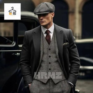 May include: A man wearing a gray three-piece suit with a black jacket, a gray vest, and gray pants. He is also wearing a gray newsboy cap and a burgundy tie.