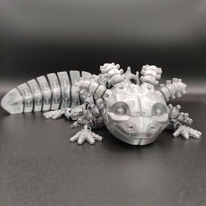 May include: A silver 3D printed robotic axolotl with a segmented tail and articulated limbs. The axolotl has a cute, cartoonish face with large eyes.