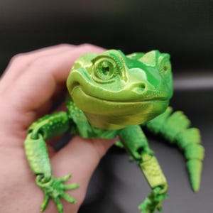 May include: A 3D printed articulated lizard figure in a vibrant lime green colour with a glossy finish. The lizard features a detailed head with prominent eyes, textured skin patterns, and segmented limbs and tail designed for movement.