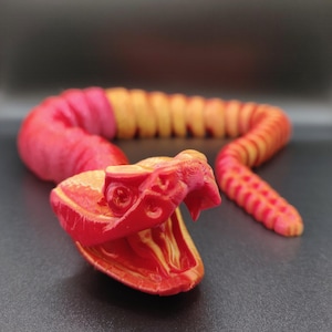 May include: A 3D printed red and yellow snake with a detailed head and a coiled body.