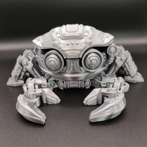 May include: A silver-coloured, mechanical crab sculpture with detailed robotic features. The crab has large, round eyes, articulated claws, and a segmented body. The design suggests a futuristic or steampunk aesthetic, with visible gears and panels.