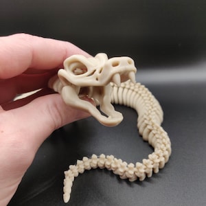May include: A beige plastic snake skeleton with a detailed skull and articulated vertebrae.