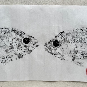 Puede incluir: Un dibujo a tinta en blanco y negro de dos peces enfrentados. Los peces tienen escamas detalladas y ojos grandes y oscuros. Un sello rojo está en la esquina inferior derecha. La obra de arte está sobre papel blanco.