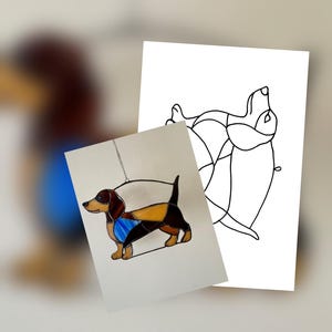 Pode incluir: Dachshund de vitral com painéis castanhos, pretos e amarelos, acentuado com uma coleira azul. A obra de arte está pendurada em um fundo branco. Um desenho a traço de um cão está ao lado da peça de vitral.