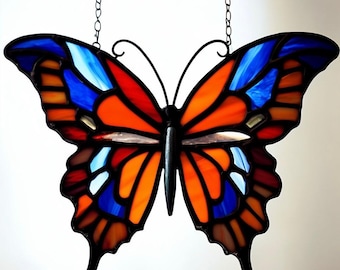 May include: A stained glass butterfly with orange, blue, and red wings. The butterfly is hanging from a chain.
