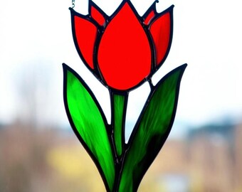 May include: A stained glass tulip with red petals and green leaves. The tulip is hanging from a chain.