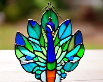May include: A stained glass peacock with a blue body, green and blue tail feathers, and an orange beak. The peacock is hanging from a wire.