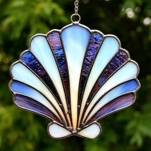 Peut inclure: Un attrape-soleil en verre coloré en forme de coquille, avec des nuances de blanc, bleu et violet. La coquille est en verre et a une finition métallique.