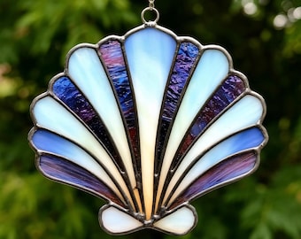 May include: A stained glass seashell suncatcher with a white, blue, and purple color scheme. The seashell is made of glass and has a metallic finish.