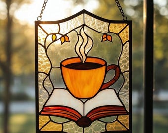 May include: Stained glass panel featuring a coffee cup with steam rising, set atop an open book. The artwork uses warm colors like orange, brown, and yellow, with a black border and chain for hanging. The background is a mix of green and gold.
