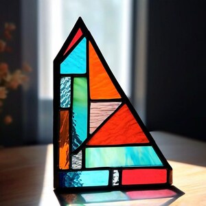 Op de afbeelding: Een glas-in-loodraam in de vorm van een driehoek met geometrische patronen in tinten blauw, groen, oranje en rood.