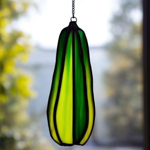 May include: A hanging stained glass ornament in a teardrop shape. The glass is a combination of green and yellow, with black lines separating the colors. The ornament is suspended by a black chain.