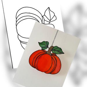 May include: A stained glass pumpkin decoration with a vibrant orange body, brown stem, and green leaves. The pumpkin is suspended by a silver chain. A line drawing of a pumpkin is in the background.