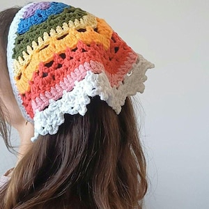 May include: A colorful, handmade crochet headscarf in a rainbow pattern. The headscarf features a spectrum of colors, including purple, blue, green, yellow, orange, pink, and white. The edges are finished with a scalloped white trim, adding a decorative touch.