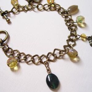 May include: A gold chain bracelet with a variety of charms, including a heart, a green stone, and several clear and yellow glass beads.