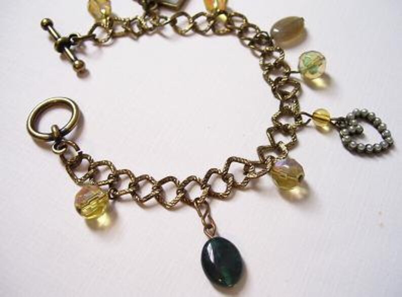 May include: A gold chain bracelet with a variety of charms, including a heart, a green stone, and several clear and yellow glass beads.