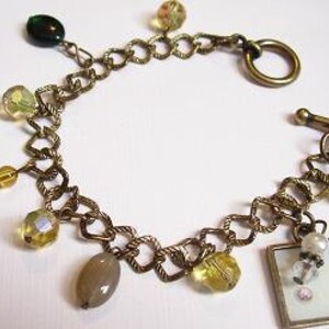 May include: A gold chain bracelet with a toggle clasp and multiple charms, including a small picture frame, a heart charm, and several clear and green glass beads.