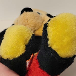 Puede incluir: Un peluche negro, amarillo y beige. El juguete tiene pies amarillos, detalles en negro y una secci&oacute;n roja. El peluche es un animal de peluche.