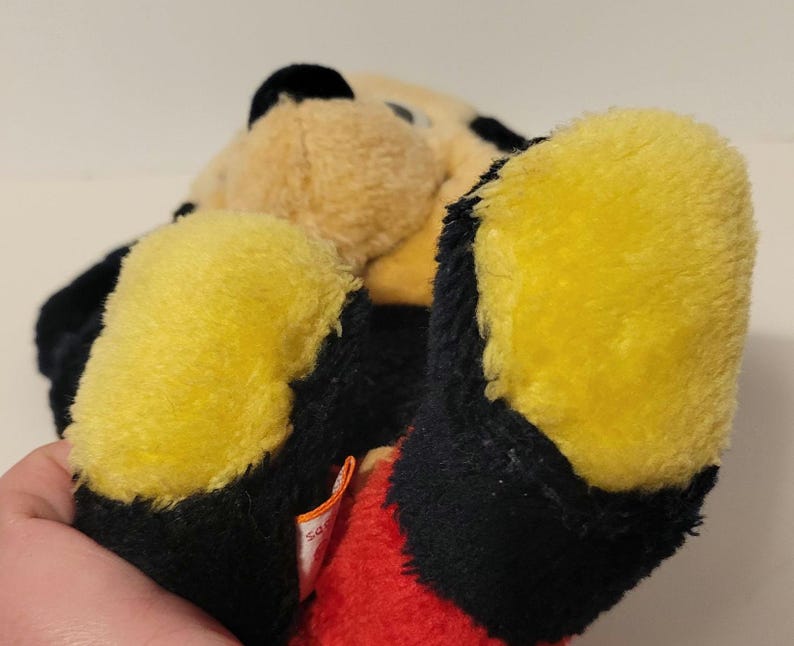 Puede incluir: Un peluche negro, amarillo y beige. El juguete tiene pies amarillos, detalles en negro y una secci&oacute;n roja. El peluche es un animal de peluche.