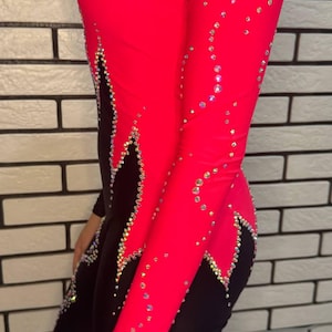 Puede incluir: Un leotardo de manga larga con un dise&ntilde;o de bloques de color rosa intenso y negro. La prenda est&aacute; adornada con numerosos cristales transparentes y reflectantes dispuestos en patrones de remolinos a lo largo de las costuras y sobre la tela.