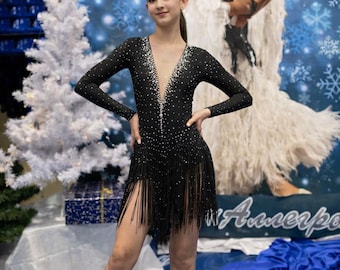 Puede incluir: Un vestido de baile negro de manga larga con un escote en V profundo, adornos de pedrería plateada concentrados en el corpiño y una falda decorada con largos flecos negros que cuelgan desde la cintura.