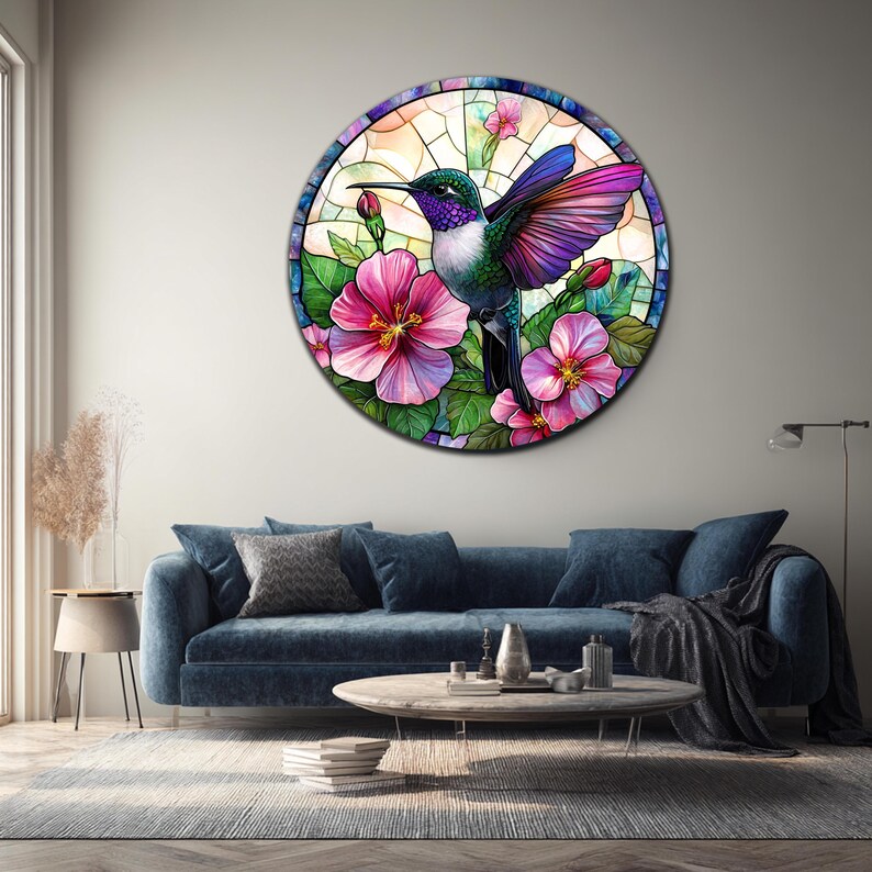 May include: Round wall art featuring a hummingbird in a stained-glass style. The bird has green, purple, and white feathers, with pink and purple wings. It is surrounded by pink hibiscus flowers and green leaves. The artwork is set against a light background.