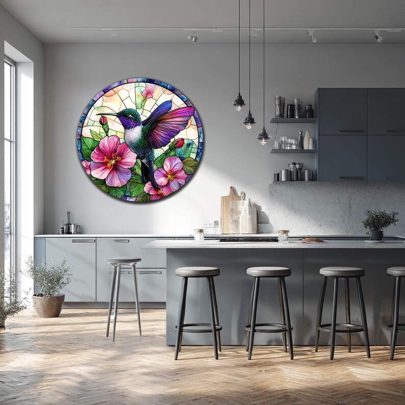 May include: Round wall art featuring a stained-glass style hummingbird with vibrant purple, green, and blue plumage. The bird is surrounded by pink hibiscus flowers and green leaves. The artwork is displayed in a modern kitchen setting.