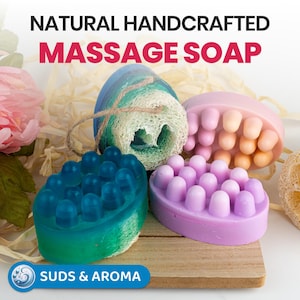 May include: Four natural handcrafted massage soaps with different colours and textures. The soaps are arranged on a wooden surface with a natural loofah sponge. The text "NATURAL HANDCRAFTED MASSAGE SOAP" is displayed above the soaps. The text "SUDS & AROMA" is displayed below the soaps.