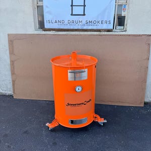 May include: Orange drum smoker on wheels with a thermometer and the text "StructureCraft Contracting LLC" on the side. The smoker is in front of a white building with a sign that reads "Island Drum Smokers Custom Built Drum Smokers".
