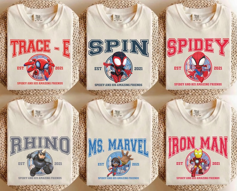 May include: Six cream-colored t-shirts featuring various Spider-Man characters and logos. Each shirt displays a different name like "Trace-E", "Spin", and "Spidey" in bold, collegiate-style lettering, along with character illustrations and the text "EST 2021".