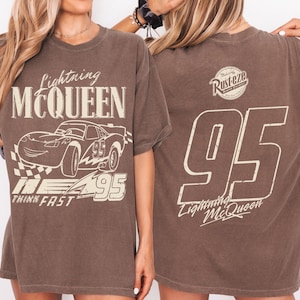 May include: Brown t-shirt with Lightning McQueen graphics. The front features the car, text "Lightning McQueen," and "Think Fast." The back displays a "Rusteze" logo and the number "95" with "Lightning McQueen."