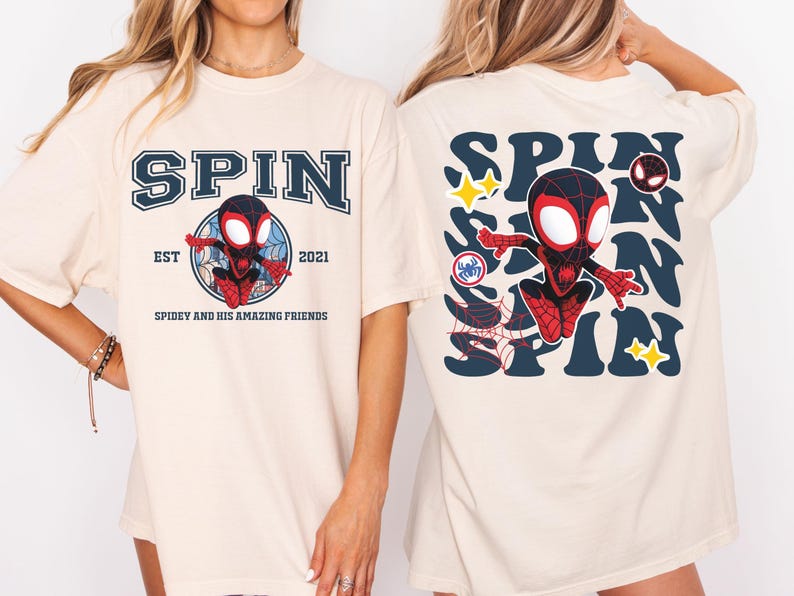 May include: Cream-colored t-shirt featuring a cartoon Spider-Man design. The front of the shirt displays the word "SPIN" above a graphic of Spider-Man, with "EST 2021" and "SPIDEY AND HIS AMAZING FRIENDS" below. The back has a larger "SPIN" design with Spider-Man and stars.