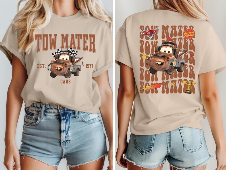 May include: Beige t-shirt featuring a graphic of Tow Mater from the Cars movie. The front design includes the text "TOW MATER EST. 1977 CARS". The back of the shirt has a larger image of Mater with the text "TOW MATER" repeated.